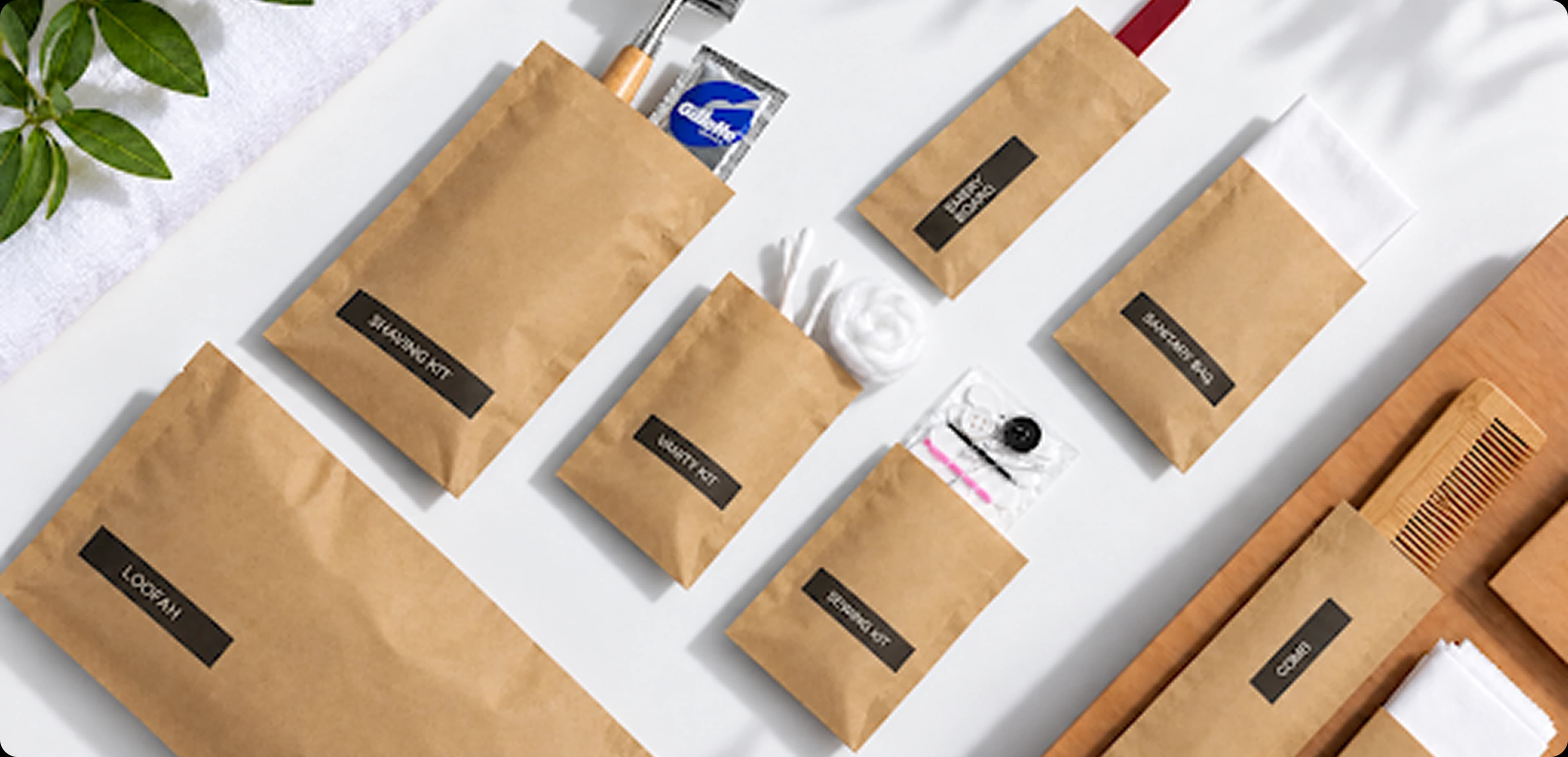 Kraft paper pouches labelled loofah, shaving kit, vanity kit, sewing kit, sanitary bag, emery board and comb, laid out on white